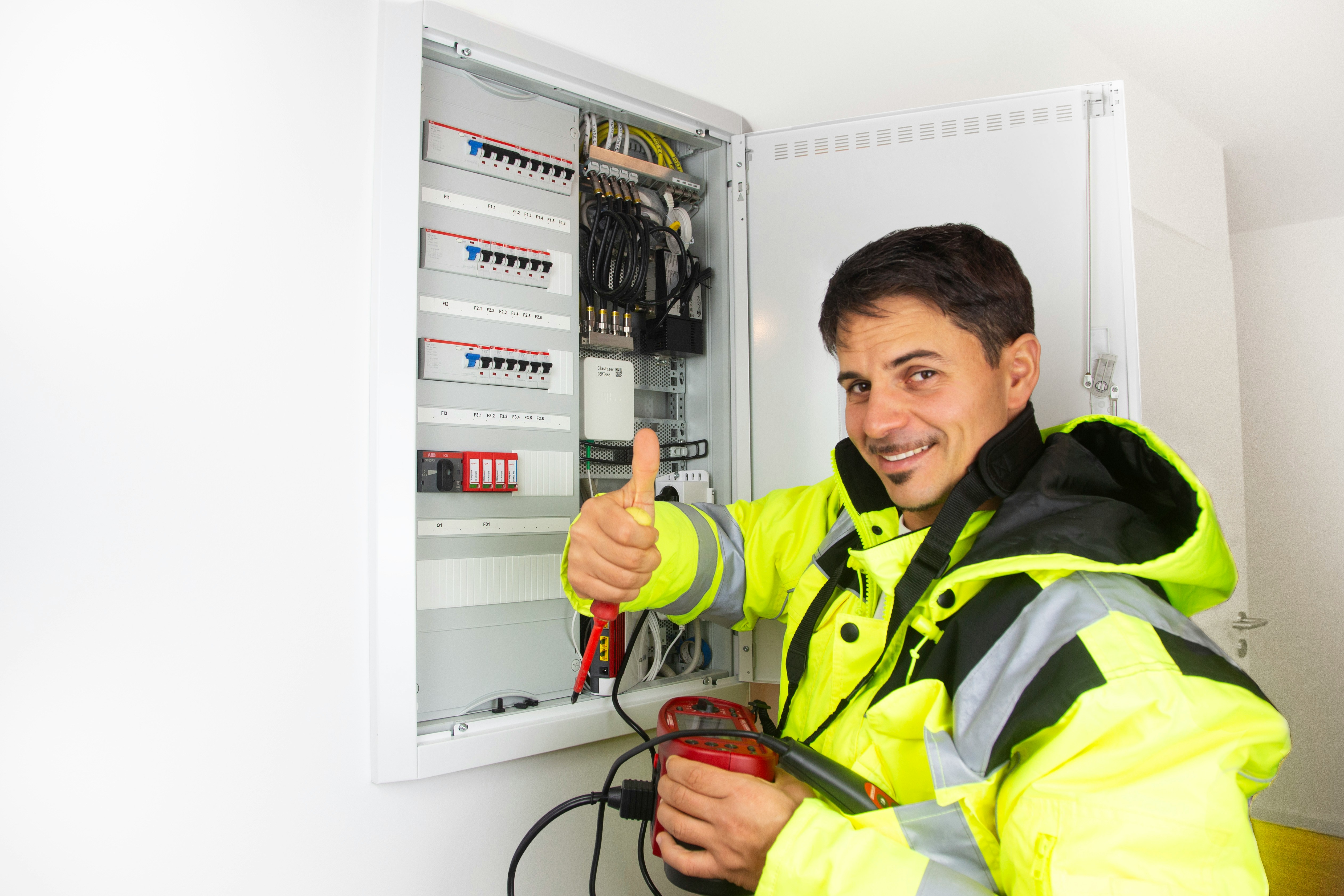Vrolijke elektricien die duimen omhoog steekt bij een geopende zekeringkast